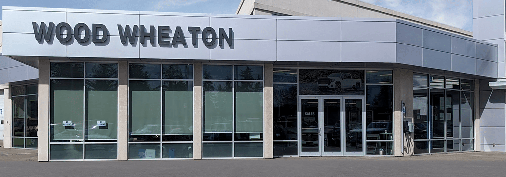 Car dealership exterior with "Wood Wheaton" signage and glass windows, including a sales entrance.