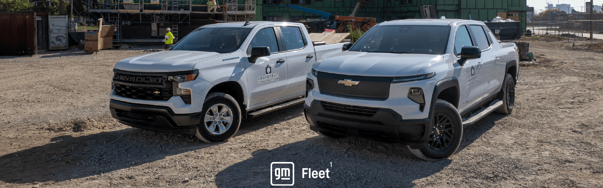 A white Chevrolet Silverado and a white Silverado EV, both lettered for a construction company, parked at a building site