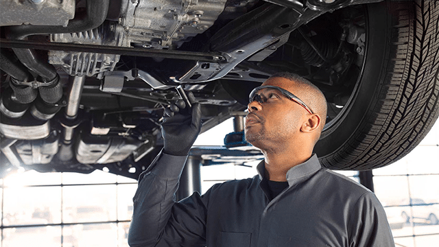 Licensed mechanic in safety glasses inspecting the underside of a vehicle raised on a hoist