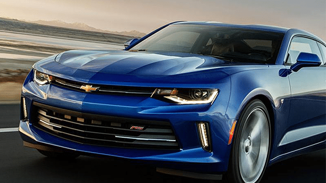Blue Chevrolet Camaro driving on an open highway at sunset