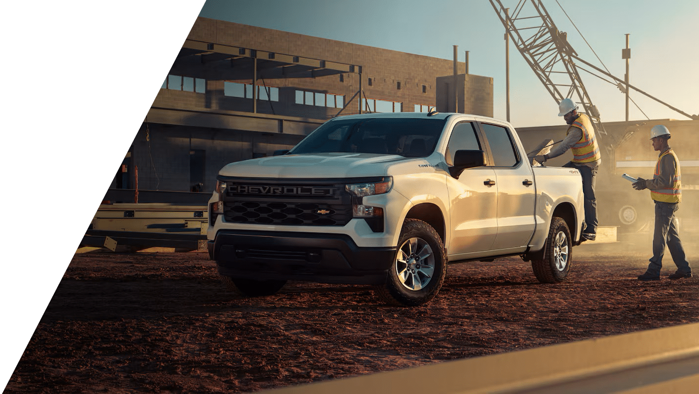 White Chevrolet Silverado work truck parked on a construction site at sunset while two workers in hard hats and high-visibility vests review plans