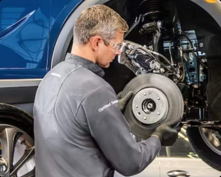 Certified Service technician removing a brake rotor from a blue van raised on a shop hoist