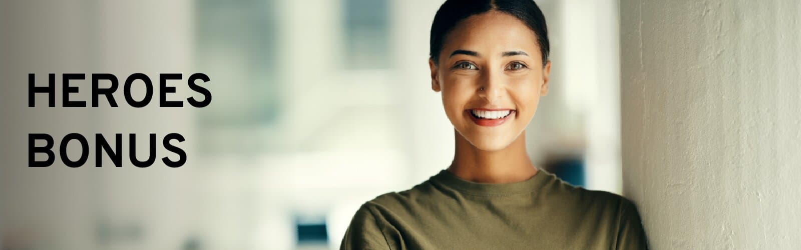Woman in an olive t-shirt smiling, leaning against a wall, under the words Heroes Bonus