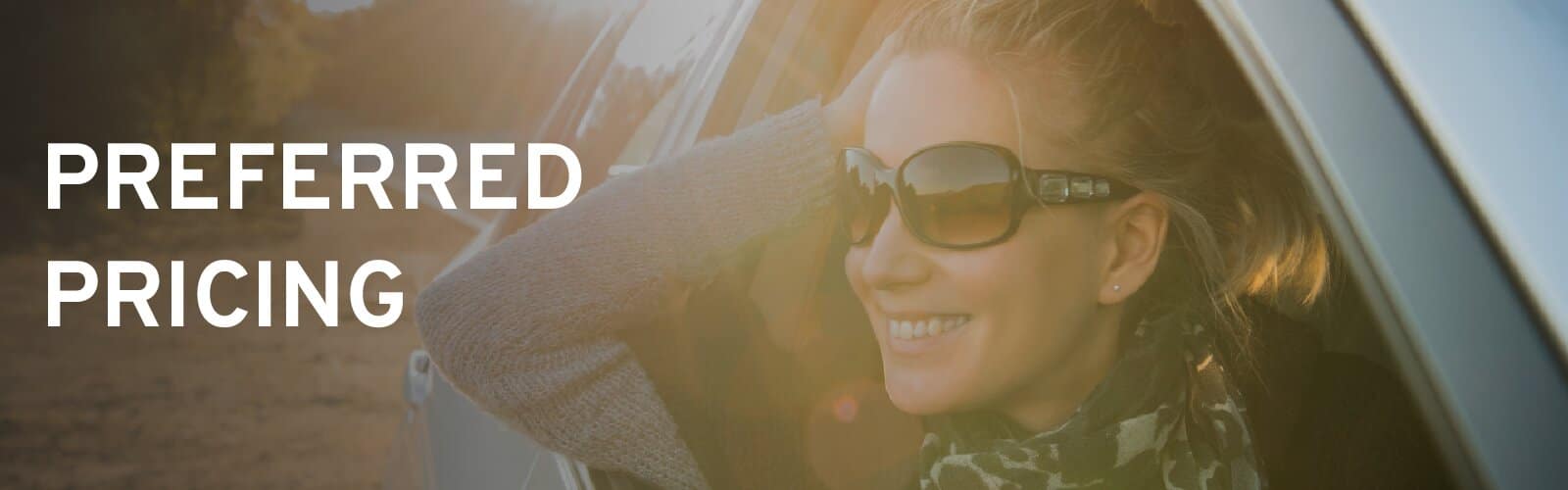 Woman in sunglasses smiling out of a car window in the late afternoon sun, under the words Preferred Pricing