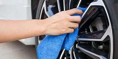 Hand wiping an alloy wheel clean with a blue microfibre cloth