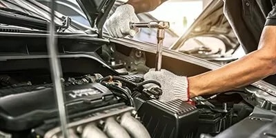 Gloved hands using a socket wrench on a car engine under an open hood